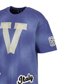 Paarse T-shirt met een groot wit "V" met tape-achtige accenten, een zwart-wit "Italië" patch, en een witte nummer "6" op de mouw.