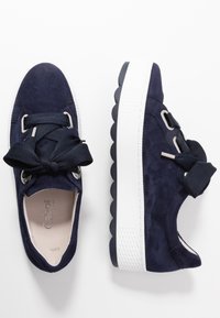 Sneakers in suede blu navy con una suola bianca spessa, caratterizzati da un design unico con lacci in grandi nastri blu navy e occhielli in argento.