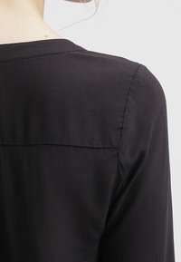 Blusa nera con una texture liscia, una vestibilità rilassata e una sottile cucitura a yoke sul retro, caratterizzata da un design semplice e classico.