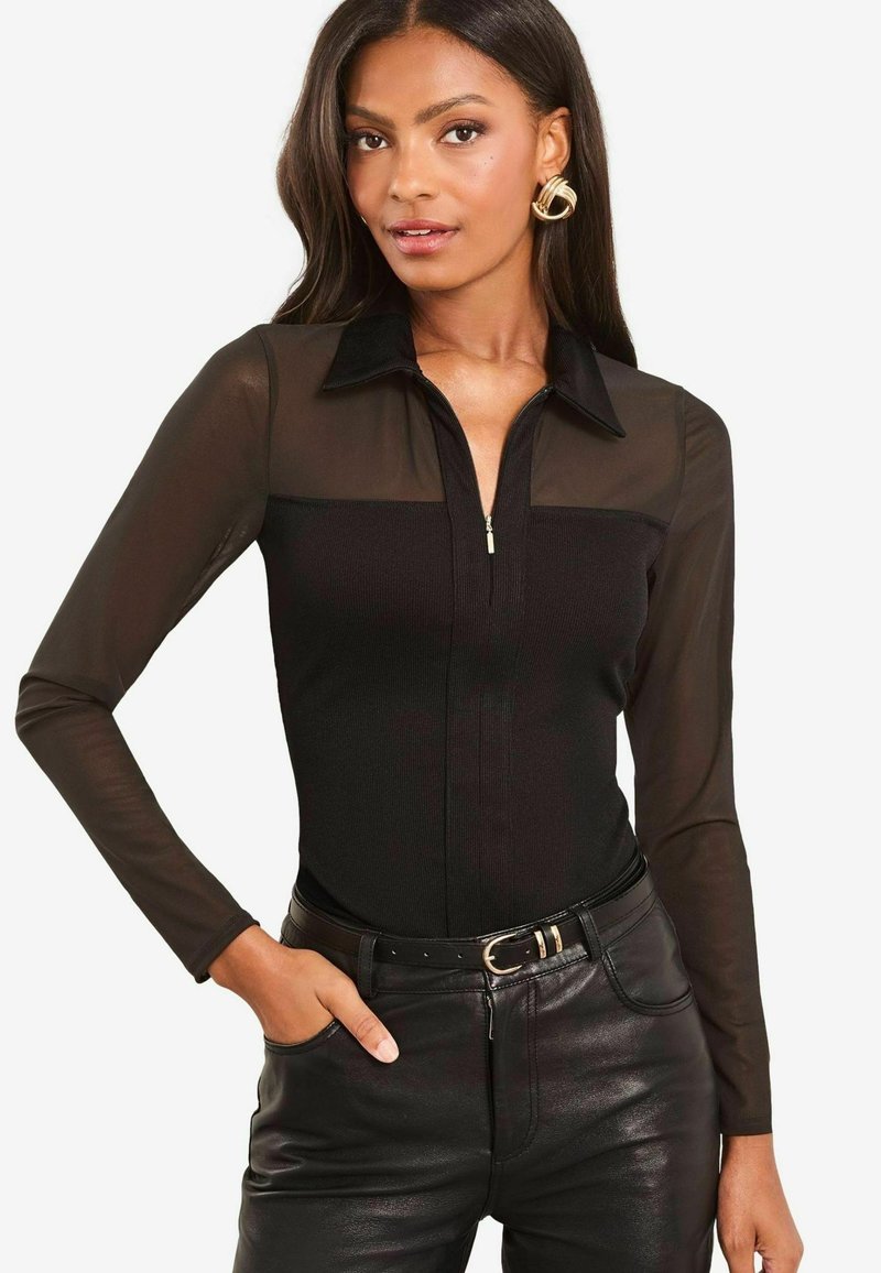 Body nero a maniche lunghe con colletto con zip, caratterizzato da pannelli in rete trasparente sulle spalle. Indossato con pantaloni di pelle neri a vita alta e una cintura.
