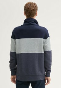 Sudadera azul marino y gris claro con cuello alto, que presenta tres bloques de color horizontales y puños de canalé. Tejido de mezcla de algodón, corte relajado.