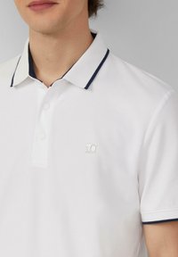 Witte polo shirt met een marineblauwe kraag en afwerking, voorzien van drie knopen en een klein logo op de linkerborst. Van katoenmix stof.