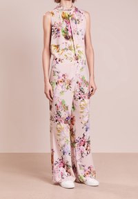 Bloemen jumpsuit van lichtroze stof, met een mouwloos ontwerp, gedrapeerde halslijn en brede pijpen versierd met kleurrijke bloemenpatronen.