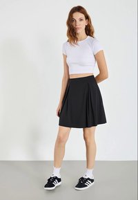 Čierna plisovaná sukňa s vysokým pásom, vyrobená z hladkej látky. Kombinovaná s bielym crop top tričkom a čiernymi športovými topánkami.