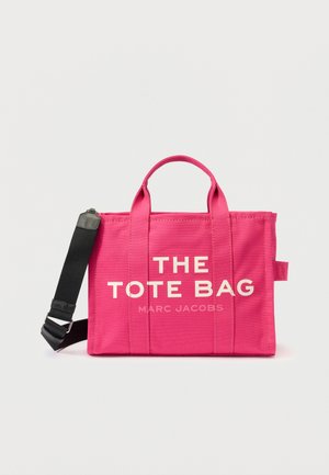 Sac en toile rose avec deux poignées supérieures et une bandoulière noire réglable. Présente un texte blanc disant "LE SAC" et "MARC JACOBS."