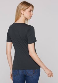 Camiseta de manga corta gris oscuro con cuello redondo, textura suave y un diseño ajustado, combinada con jeans azules que tienen costuras decorativas.