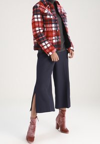 Rød og marineblå ternet jakke, tekstureret stof; grå top; marineblå cropped bukser med sideslids; lyserøde ankelstøvler med chunkytyper.