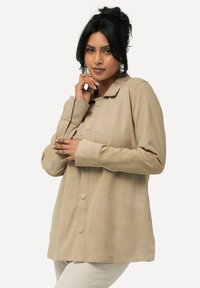 Beige Wildlederjacke mit Kragen, langen Ärmeln und Knopf-Frontverschluss. Sanfte Textur und lässige Passform.