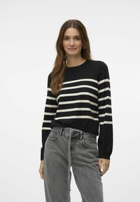 Zwarte en crème gestreepte trui met een ronde halslijn en lange mouwen, gecombineerd met grijze spijkerbroek met hoge taille. Zachte textuur, casual design.
