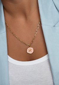 Goldkettenhalsband mit einem unregelmäßigen Sechseck-Anhänger, der eine pinkfarbene Emaille-Oberfläche und ein erhabenes Seestern-Design aufweist.