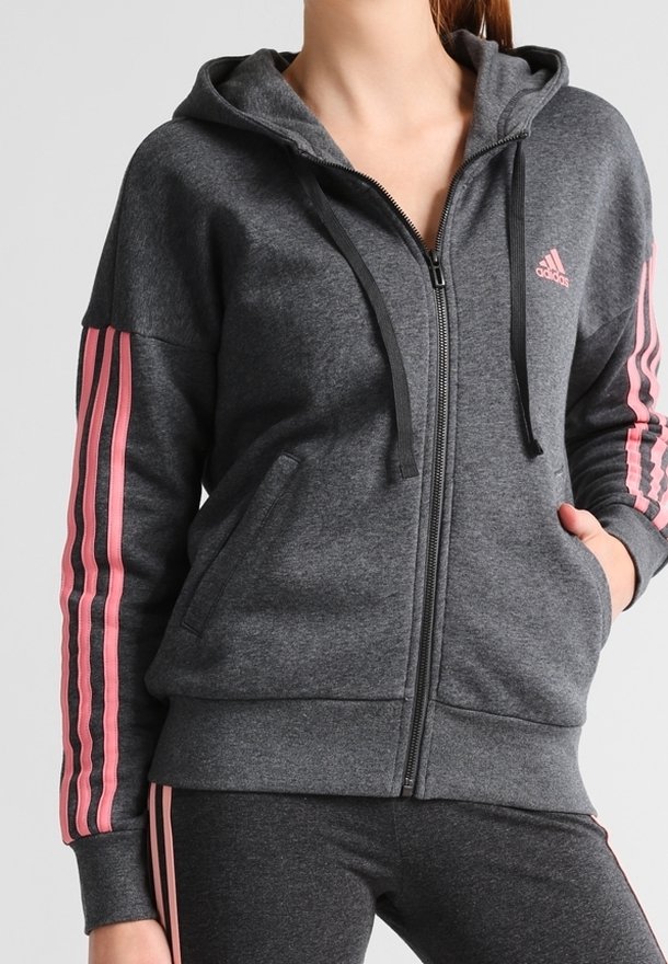Sweat à capuche zippé gris avec une capuche, featuring des accents roses à trois rayures sur les manches et les poches avant, fabriqué en tissu doux et texturé.