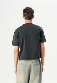 Tricou scurt negru din bumbac, cu mâneci scurte și guler rotund, asortat cu pantaloni din denim verde deschis, având buzunare la spate.