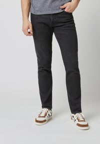 Jeans de mezclilla ajustados en un gris oscuro con una textura sutil y diseño de cinco bolsillos, combinados con zapatillas deportivas blancas y marrones.