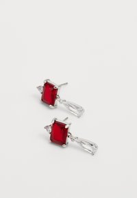 Pendientes rectangulares rojos con acentos en forma de lágrima transparentes y montura de metal plateado. Presenta engastes de cuatro garras para las piedras principales.