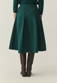 Rohelise värviga plisseeritud puuvillast seelik, keskmise vasikasääre pikkusega, siledapinnaline ja varjatud lukuosaga, koos pruunide põlvekõrgete saabastega.