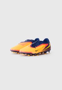 Des chaussures de football jaune vif avec des accents bleu marine, une tige texturée et un logo Nike noir. Elles possèdent une semelle extérieure pour terrain ferme avec des crampons orange.