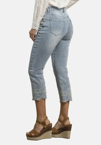 Vaqueros capri de mezclilla azul claro con dobladillo bordado en forma de ondas. Combinados con sandalias de cuña color tostado, que exhiben un acabado texturizado y un diseño resistente.