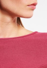 Strukturiertes Strickoberteil in einem weichen Roseton mit weitem Ausschnitt und kurzen Ärmeln, Nahaufnahme des Stoffs und Schulterbereichs.