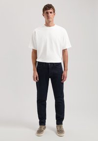 Camiseta de algodón blanca de manga corta combinada con jeans de mezclilla azul oscuro y zapatillas grises, con un corte estándar y un diseño minimalista.