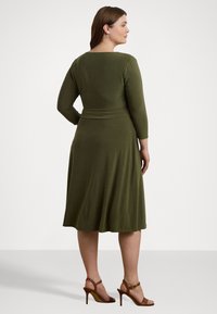 Ελαιόλαδο πράσινο φόρεμα σε μαλακό ύφασμα, με τρία τέταρτα μανίκια και εφαρμοστή μέση που ανοίγει στο τελείωμα. Συνδυασμένο με καφέ σανδάλια με τακούνι.