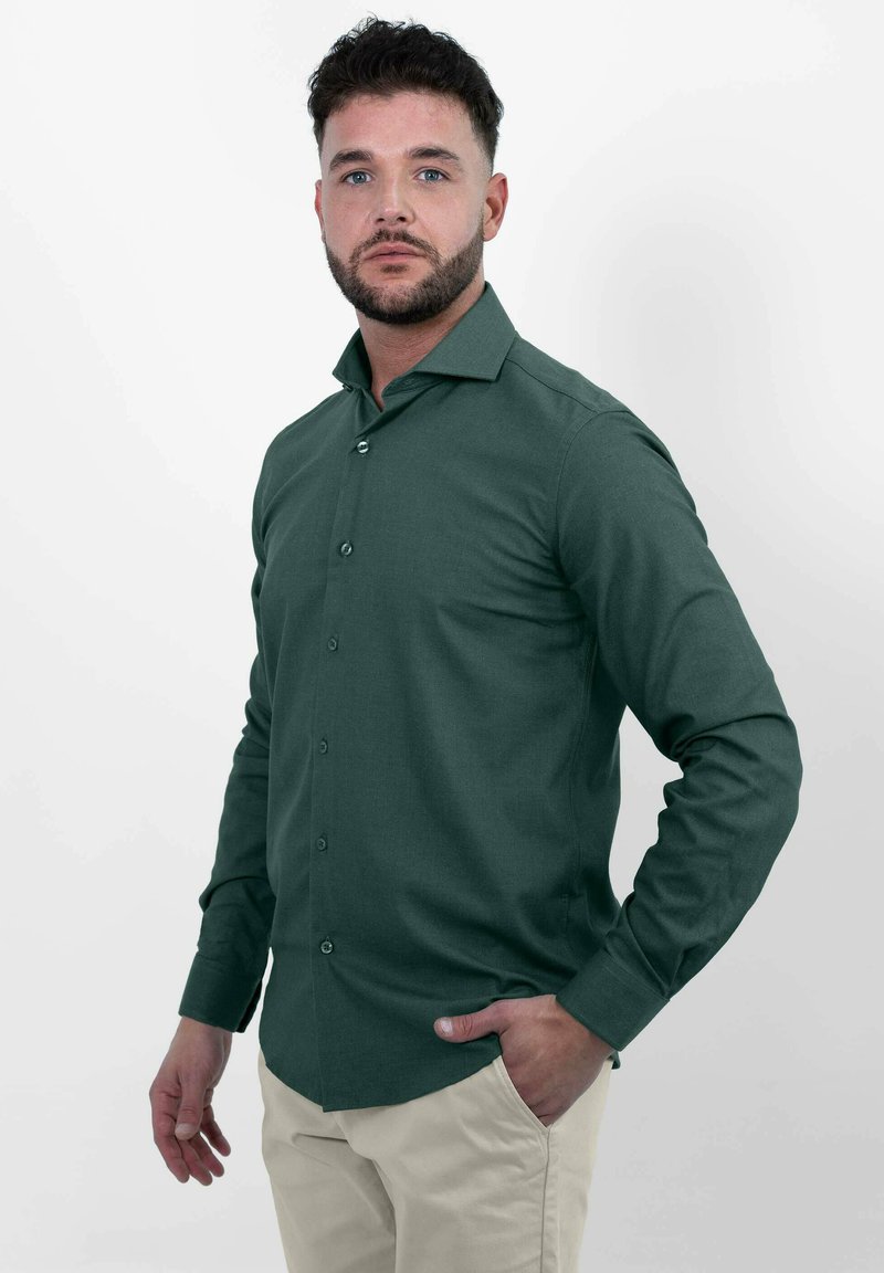 Groene lange mouw knoop-overhemd gemaakt van gladde stof, met een puntige kraag en een knoopsluiting aan de voorkant, gecombineerd met lichtgekleurde broeken.