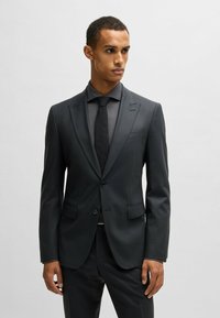 Completo su misura grigio scuro con rever a punta, chiusura con un solo bottone, due tasche frontali, design slim-fit e tessuto strutturato.