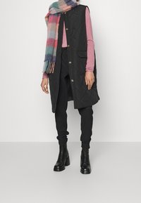 Musta tikattu liivi kultaisilla nappeilla, päällä vaaleanpunainen pitkähihaisen paita, yhdistetty mustiin housuihin ja mustiin nauhallisiin saappaisiin. Monivärinen raidallinen huivi.