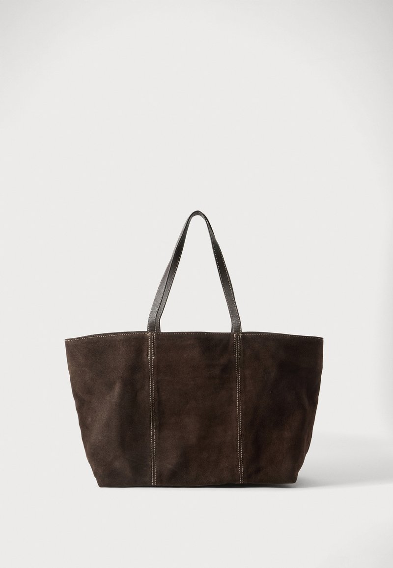 Sac cabas en daim brun foncé avec deux poignées en cuir noir et des détails de coutures verticales, présenté sur un fond clair uni.