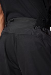 Shorts de sport noirs avec une texture lisse, dotés d'une taille élastique et d'un cordon de serrage pour un ajustement. Logo de la marque visible.