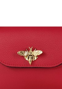 Rode lederen handtas met een gestructureerde afwerking, voorzien van een gouden bijenklip als opvallend accent. Het ontwerp omvat een gebogen klep en contrasterende stiksels.