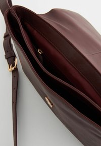 Sac à main en cuir marron avec une texture lisse, doté d'un fermoir doré et d'une bandoulière réglable. L'intérieur présente deux compartiments doublés de tissu.