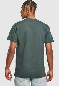 T-shirt di cotone verde scuro con maniche corte, colletto a giro e orlo dritto. Tessuto liscio, senza motivi visibili. Modello di spalle.