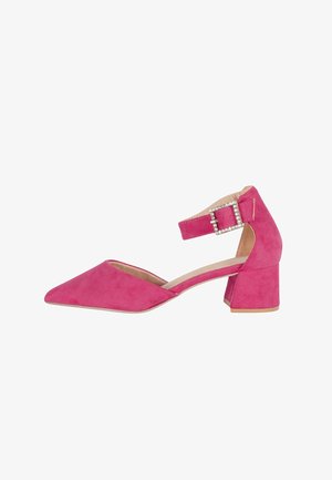 Scarpa bassa in camoscio rosa con punta affusolata, cinturino alla caviglia e fibbia decorata con strass su sfondo bianco.