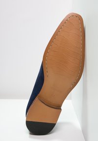 Semelle de chaussure en daim bleu marine avec une incrustation en cuir lisse couleur tan, présentant une finition texturée et un talon en caoutchouc noir pour une meilleure adhérence. Taille 42 indiquée.
