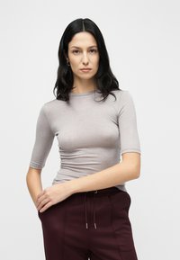 T-shirt gris clair ajusté avec manches courtes et col rond ; texture lisse, porté avec un pantalon taille haute bordeaux à cordon de serrage.