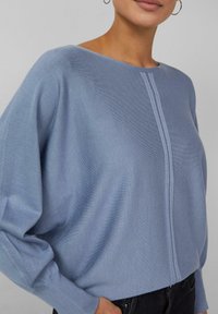 Hellblauer Strickpullover mit entspannter Passform, weitem Ausschnitt und langen Ärmeln. Er verfügt über eine dezente mittige Naht und eine gerippte Struktur.