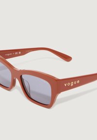 Ochelari de soare din plastic roșu cu rame rectangulare, lentile întunecate și branding aurie "vogue" pe vrejsuri. Finisaj neted și design modern.