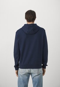 Felpa blu navy con una texture morbida, caratterizzata da un cappuccio standard e maniche lunghe. L'orlo è elasticizzato e si abbina a jeans blu chiaro.