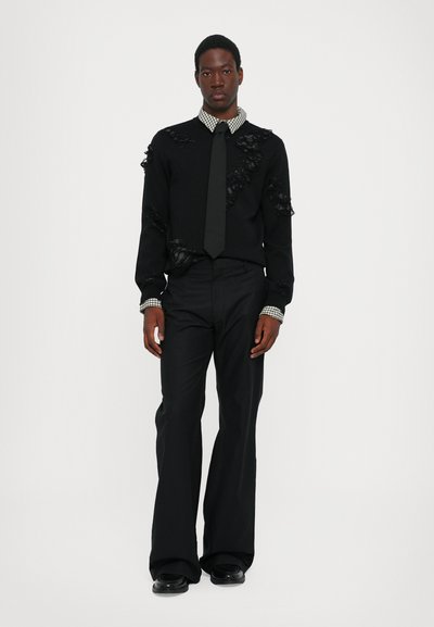 Pull noir avec une texture usée, mettant en avant des accents floraux. Associé à un pantalon noir évasé et un col de chemise à carreaux. Détails en cravate noirs.