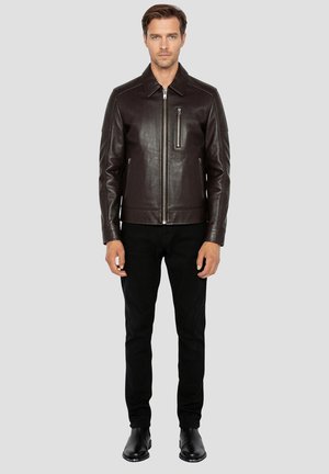 Bruine leren jas met een voorzijde rits, opstaande kraag, zijzakken en een met rits afsluitbare borstzak. Draag dit met een zwarte broek en laarzen.