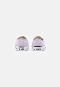 Alacsony profilú, levendula színű vászon sportcipők fehér fűzőkkel, fekete gumitalppal és a sarokon található "Converse All Star" logóval.