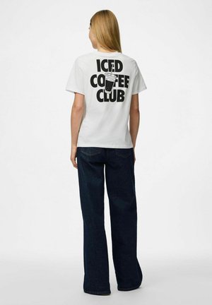 T-shirt blanc avec un grand texte noir "ICED COFFEE CLUB" et un graphique d'un gobelet de boisson dans le dos. Associé à un jean ample bleu foncé.