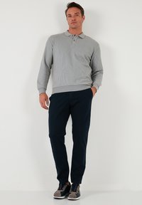 Pulover gri deschis cu dungi, cu guler, asociat cu pantaloni tapered de nuanță bleumarin închis și pantofi gri. Design minimalist, croială casual.
