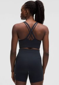 Fekete sportmelltartó keresztezett pántokkal, hozzáillő magas derekú shortssal párosítva. Simára kidolgozott, elasztikus anyagból készült a kényelem érdekében.