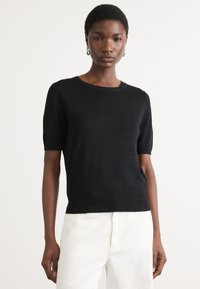 Black short-sleeve sweater made of soft fabric with a ribbed neckline and hem. Features a fitted silhouette and smooth texture.