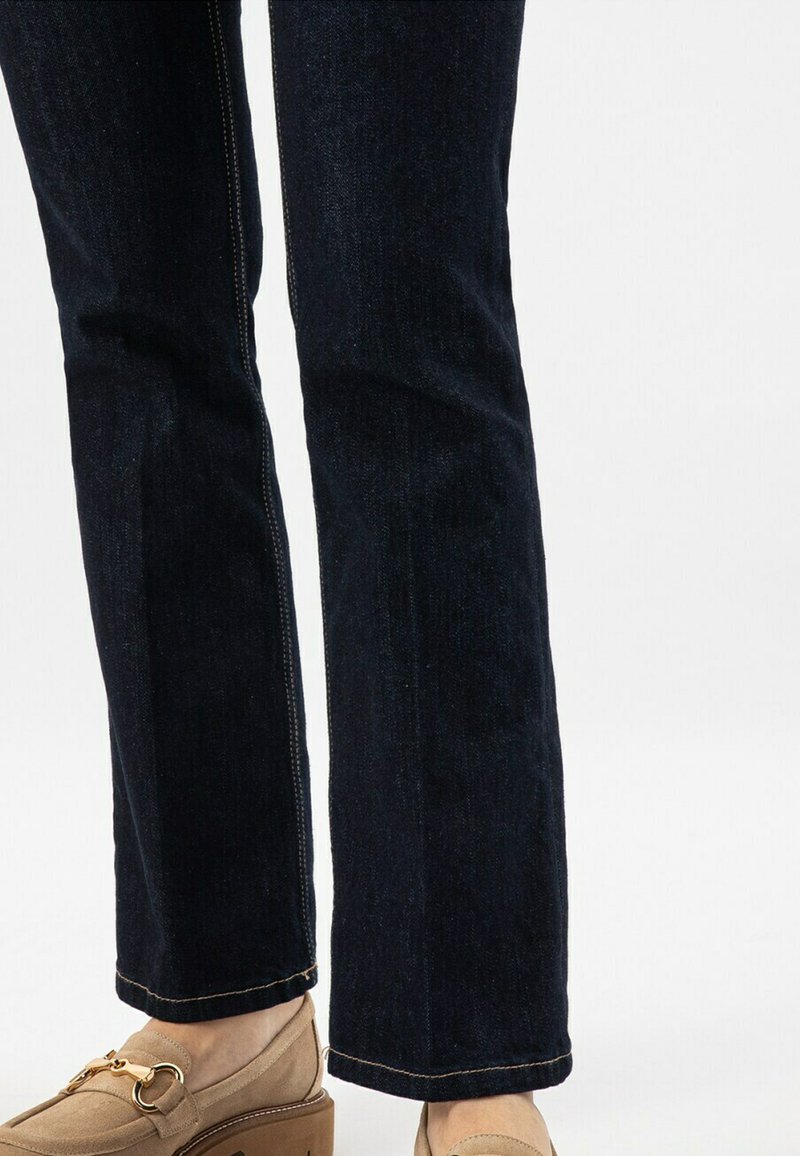 Dunkelblaue Jeans im geraden Schnitt, mit sichtbarer Naht, einem sauberen Saum und einer dezenten Textur, kombiniert mit beigen Slippers.