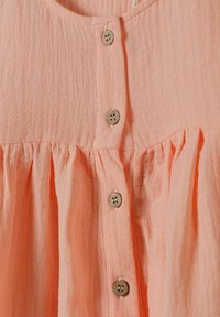 Blouse en coton couleur pêche avec une surface texturée, dotée d'un col rond, de fermetures à boutons et de détails froncés à la taille.
