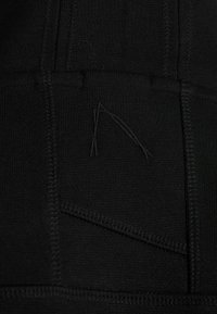 Tela negra, con costuras texturizadas y un patrón geométrico. Un detalle notable incluye un diseño de costura sutil y contrastante.