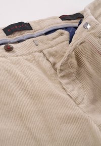 Beige Cord-Hosen mit Reißverschluss, Knopfverschluss und gestreiftem Bund. Sie zeichnen sich durch eine Textur mit feiner Rippung und dekorativen Nähten aus.