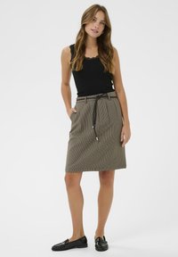 Jupe crayon à carreaux marron avec une taille élastiquée, associée à un débardeur noir avec des bordures en dentelle et des mocassins noirs.